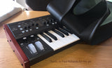 A Behringer Deepmind synthesizer with a black dust cover placed on it, showing the synthesizer's keyboard and knobs.