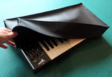 A black vinyl dust cover being placed on a Behringer MS-1 Synthesizer, showing the cover's fit around the keyboard and synthesizer controls.